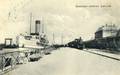 170119, Afbeelding van het stoomschip R. van Hasselt van Rederij Koppe langs de kade van de haven te Stavoren, met rechts het H.S.M.-station Stavoren en een sneltrein uit Leeuwarden met overstappende reizigers.