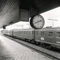 167741, Afbeelding van de stationsklok op het eerste perron van het N.S.-station Driebergen-Zeist te Driebergen-Rijsenburg, met op de achtergrond een getrokken trein bestaande uit rijtuigen plan E en plan K., Nederlandse Spoorwegen, fotograaf