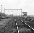 167136, Afbeelding van de zuidzijde van het emplacement van het N.S.-station Elst te Elst (Elst aansluiting), gezien in de richting Nijmegen, met de spoorwegovergang in de Bemmelseweg en het seinhuis Post T., Nederlandse Spoorwegen, fotograaf