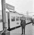 824851, Afbeelding van een conducteur van de N.S. in het nieuwe conducteursuniform op het perron van het N.S.-station Woerden. Op de achtergrond een electrisch treinstel plan V (mat. 1964) van de N.S. in de nieuwe huisstijl.