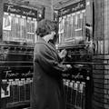 849573, Afbeelding van een vrouw bij de automaten voor nylon kousen in de hal van het N.S.-station Hilversum., Nederlandse Spoorwegen, fotograaf