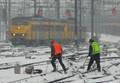 801335, Afbeelding van twee wegwerkers van Volker Stevin Rail & Traffic op het besneeuwde emplacement van het N.S.-station Utrecht Centraal te Utrecht, tijdens het sneeuwvrij maken van wisseltongen. Op de achtergrond een naderende trein., Lansink, V.M., fotograaf