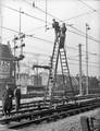 400065, Afbeelding van wegwerkers van de N.S. op een rolladder tijdens de werkzaamheden ten behoeve van de electrificatie van het Centraal Station te Utrecht, met op de achtergrond de bebouwing aan de Leidseweg en de Leidsekade., Onbekend